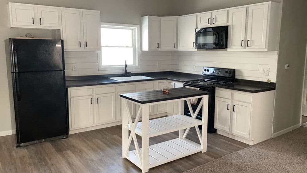 Modern kitchen with white cabinets, black countertops, and a central dining island.