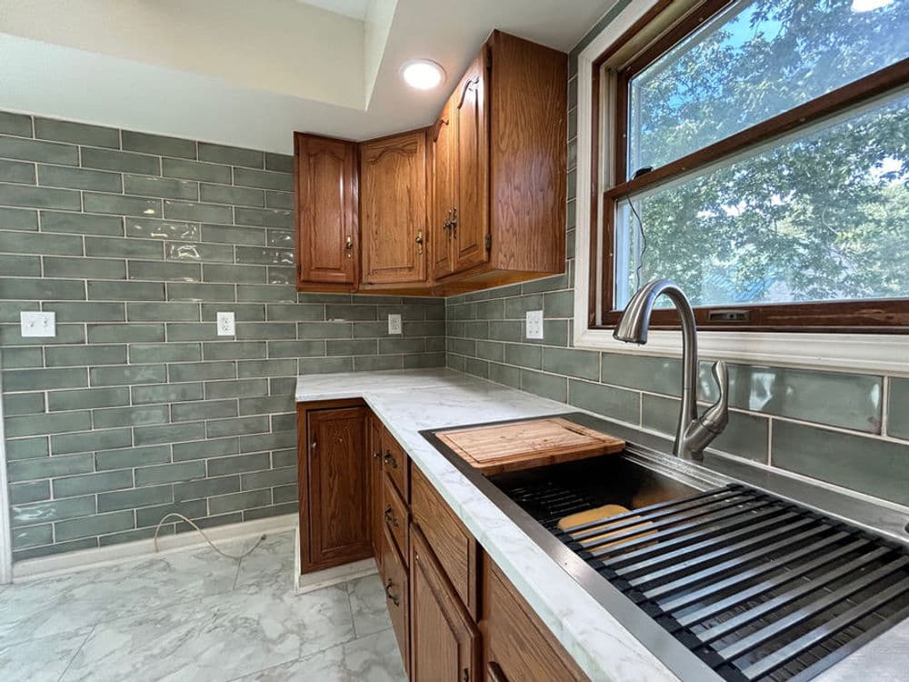 Modern kitchen with wooden cabinets, green subway tile, and marble countertop. Bright and stylish.