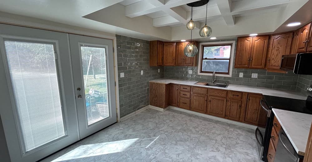 Light-filled modern kitchen featuring oak cabinetry, marble flooring, and sliding glass door.