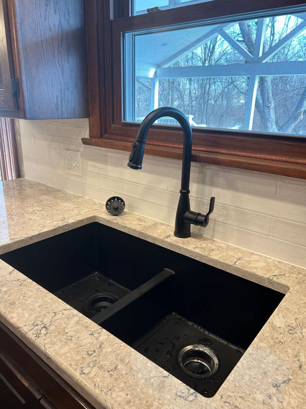 Black double sink with modern faucet and granite countertop in a kitchen. Natural light from window.