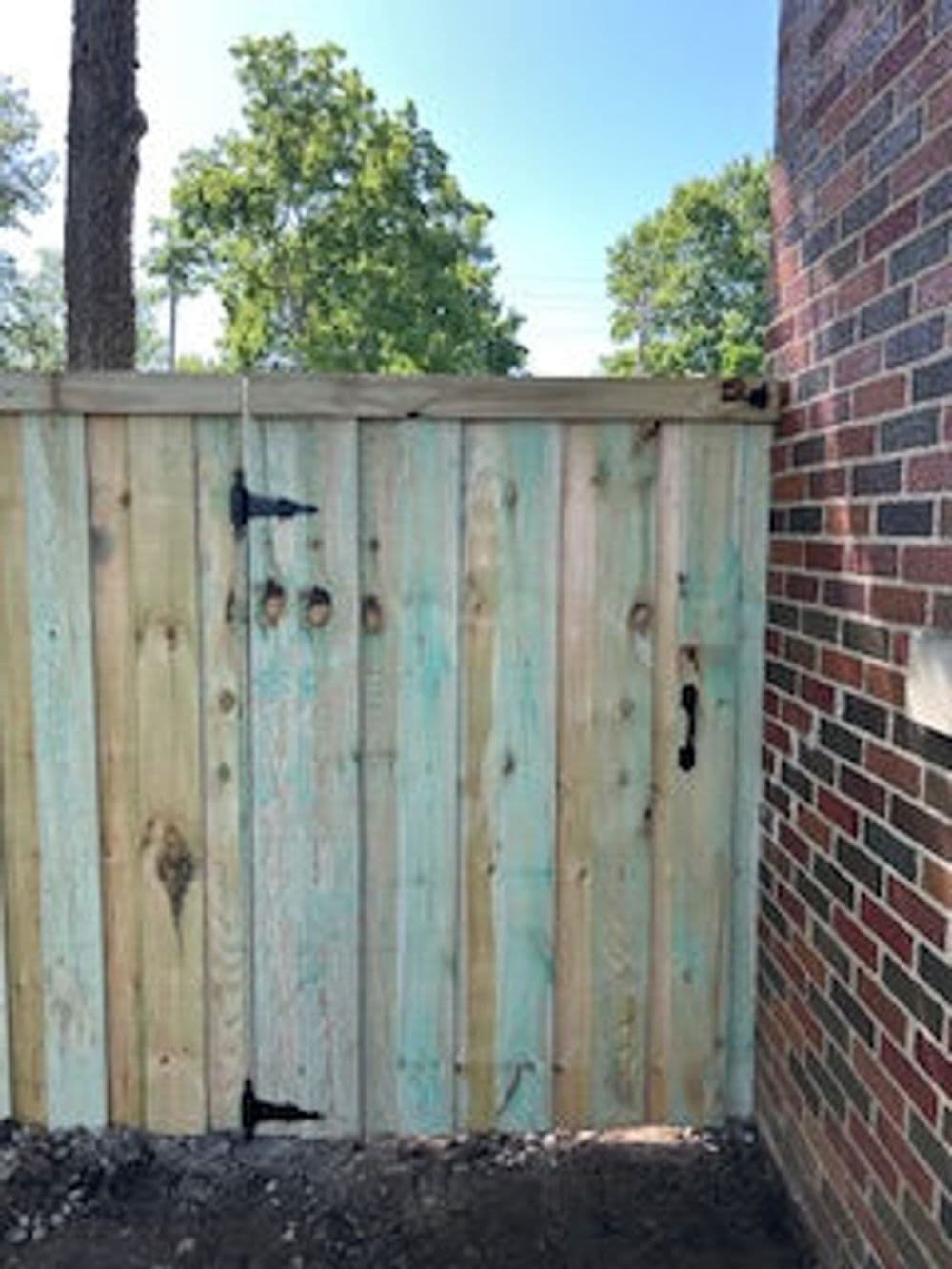 Wooden gate with green accents next to a brick wall and trees in the background.