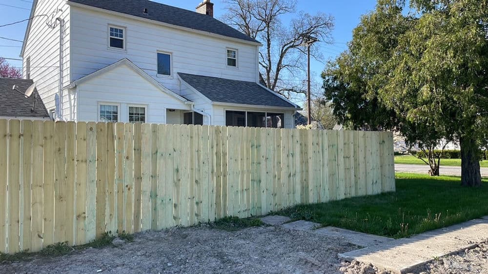 White two-story house with a new wooden fence and grassy yard on a sunny day.