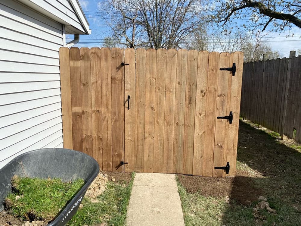 Wooden garden gate with black hardware beside a concrete path and grass area.