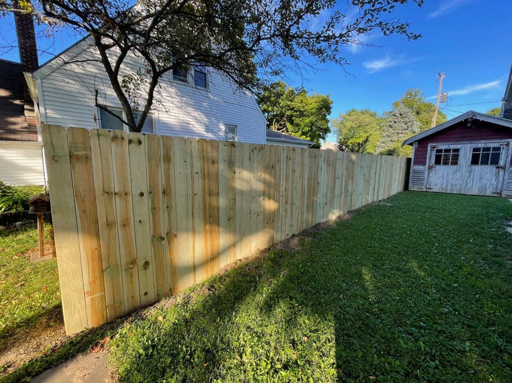 New wooden privacy fence in a backyard with green grass and clear blue sky.