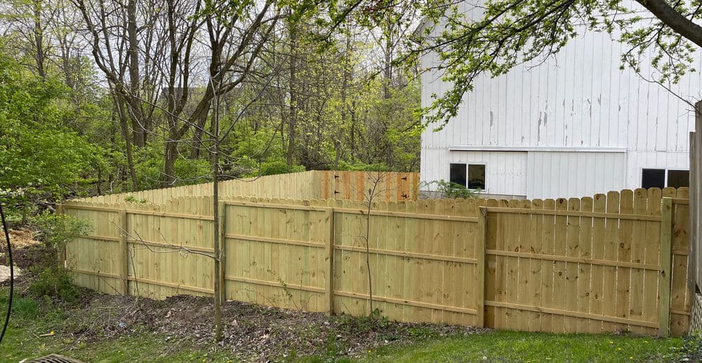 Newly installed wooden fence surrounding a backyard with green trees and a white house.
