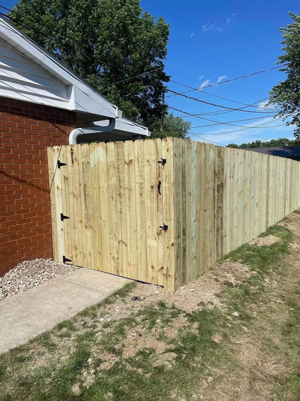 New wooden privacy fence with gate beside a brick house, featuring sunny blue skies.