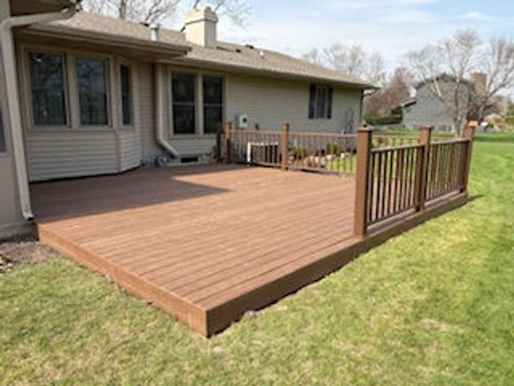 Elegant wooden deck with railings beside a home and green lawn under a clear sky.