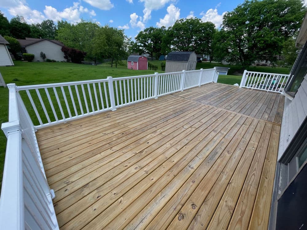 Spacious wooden deck with white railing and green lawn under a blue sky.