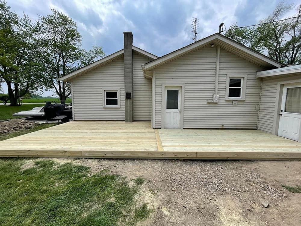 Newly constructed wooden deck adjacent to a residential home, surrounded by greenery.