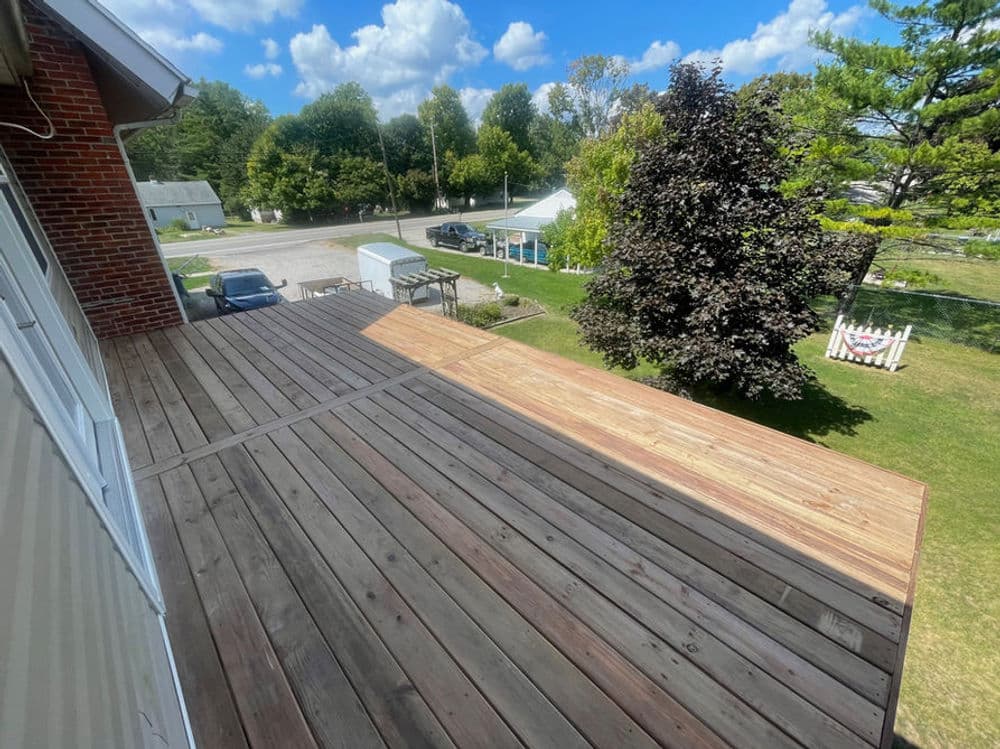 Wooden deck with sunlight and green surroundings in a residential area under a blue sky.