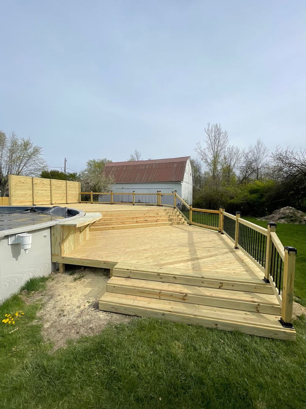 New wooden deck surrounding a pool, with steps and a view of a barn in the background.
