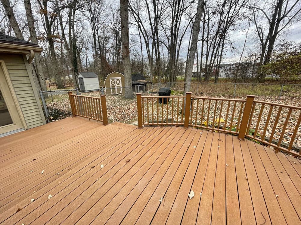 Newly built wooden deck with railing overlooking a wooded area and storage shed.