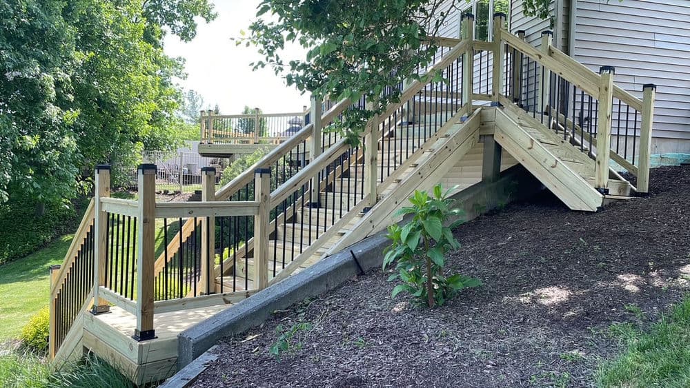 Wooden wheelchair-accessible ramp with railings, surrounded by greenery and landscaping.