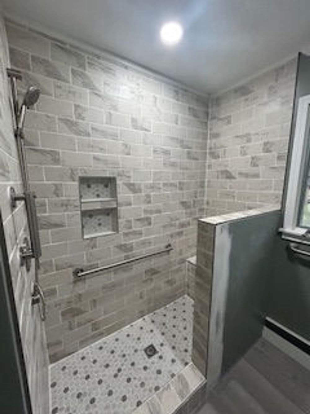 Modern walk-in shower with gray tiled walls, soaking area, and built-in shelving.