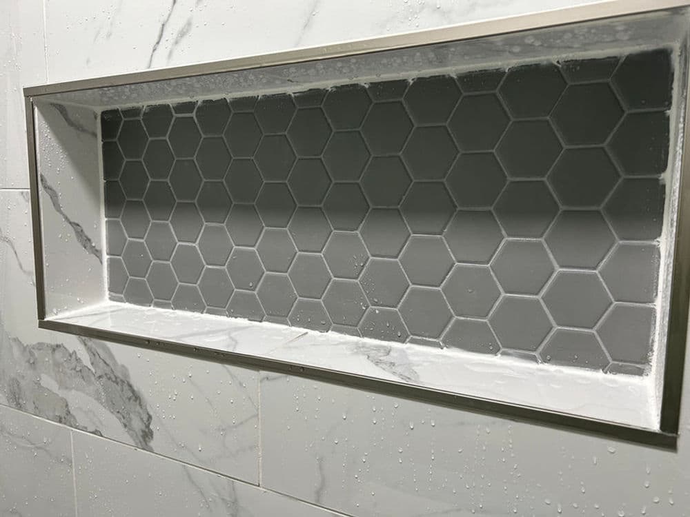 Hexagon tile shower niche with marble accents and water droplets, designed for modern bathrooms.