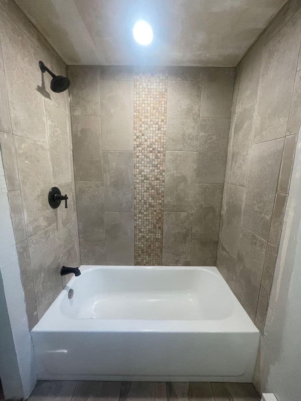Modern bathroom with a white bathtub, mosaic tile accent wall, and black fixtures.
