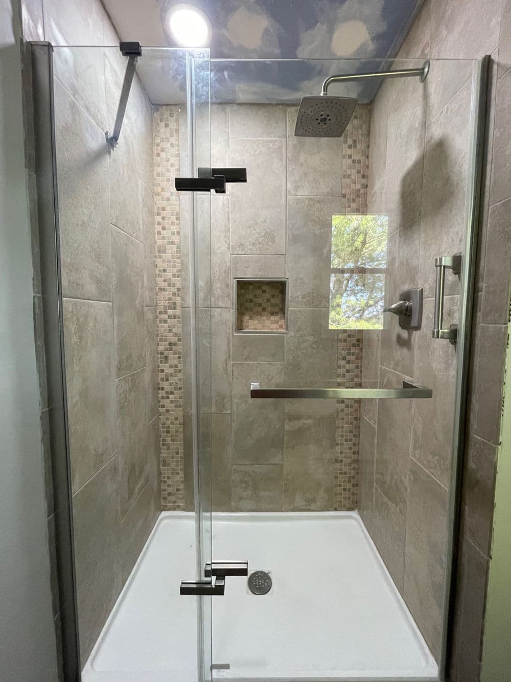 Modern glass shower with tiled walls, rainfall showerhead, and built-in shelf.