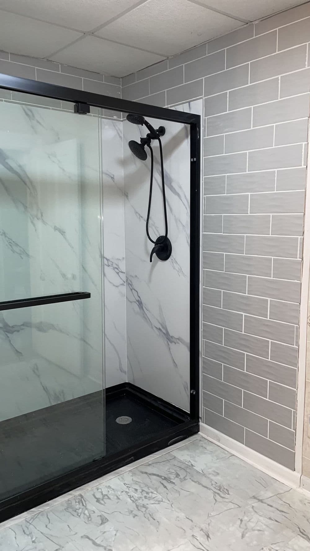 Modern shower enclosure with marble-patterned walls and sleek black fixtures.