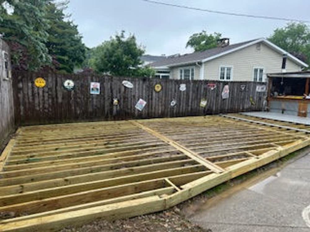 Construction site of a wooden deck with framing in a backyard, cloudy weather.