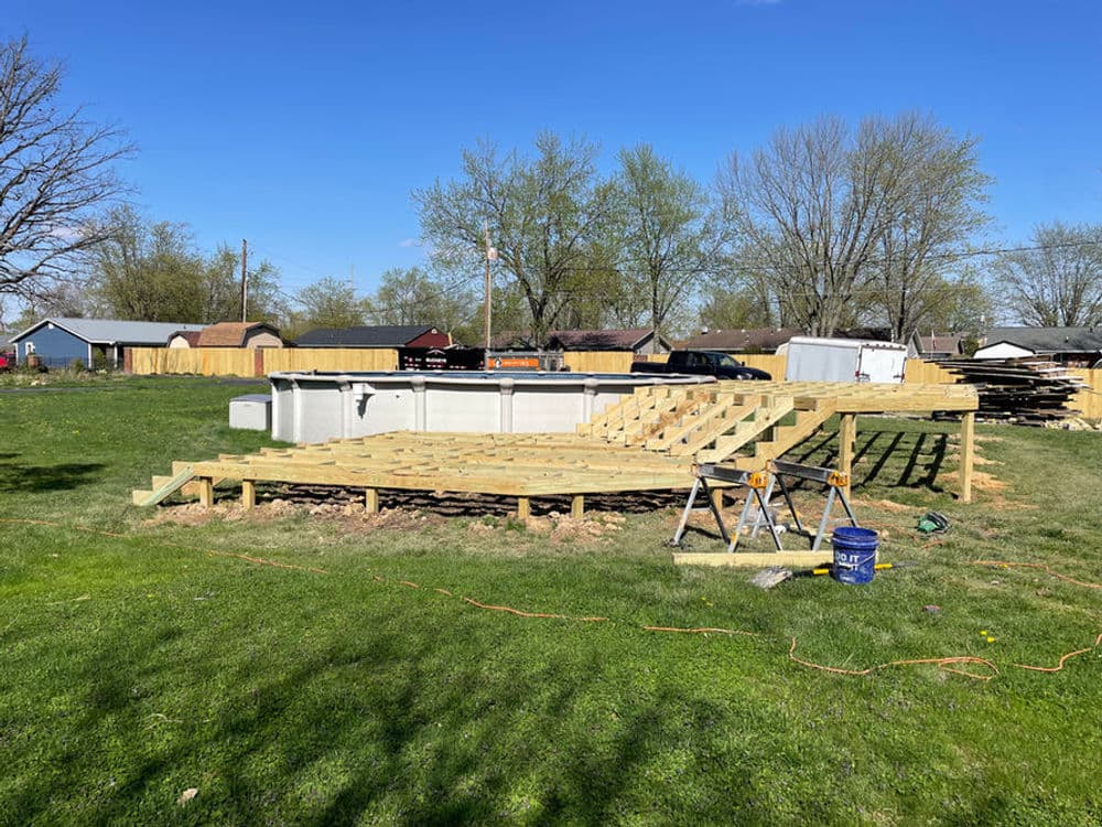 Construction of an above-ground pool with wooden deck in a residential backyard on a clear day.