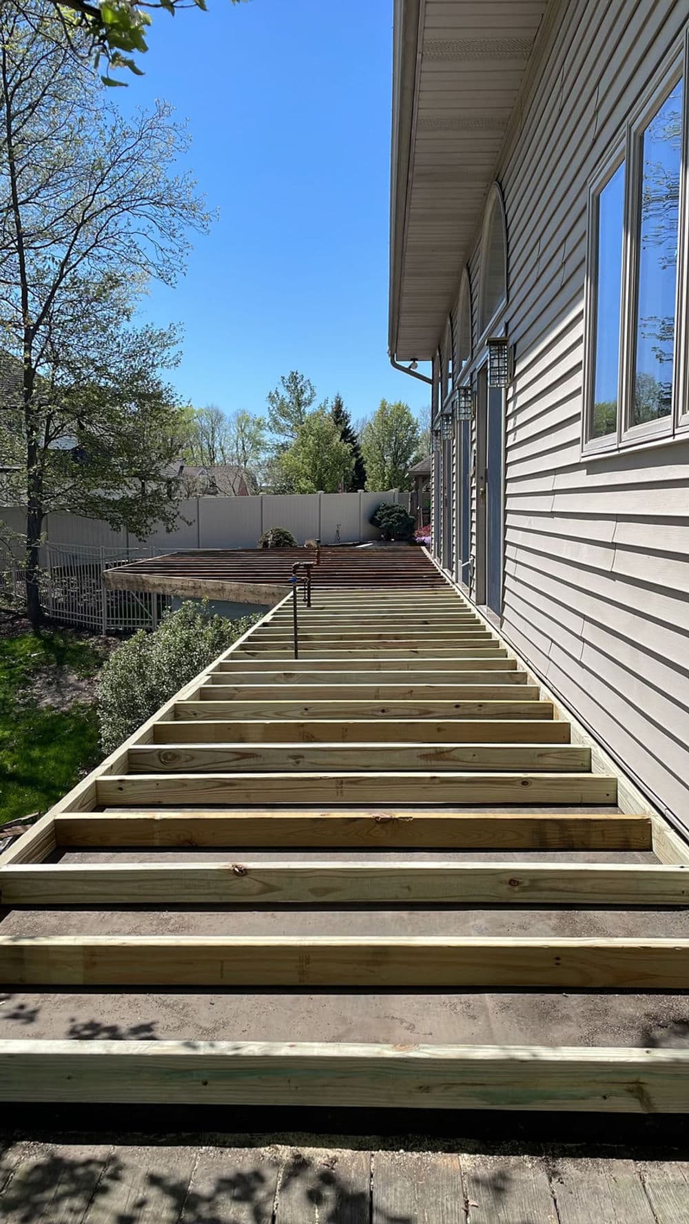 Newly constructed wooden deck frame alongside a house on a sunny day, showcasing under-construction.