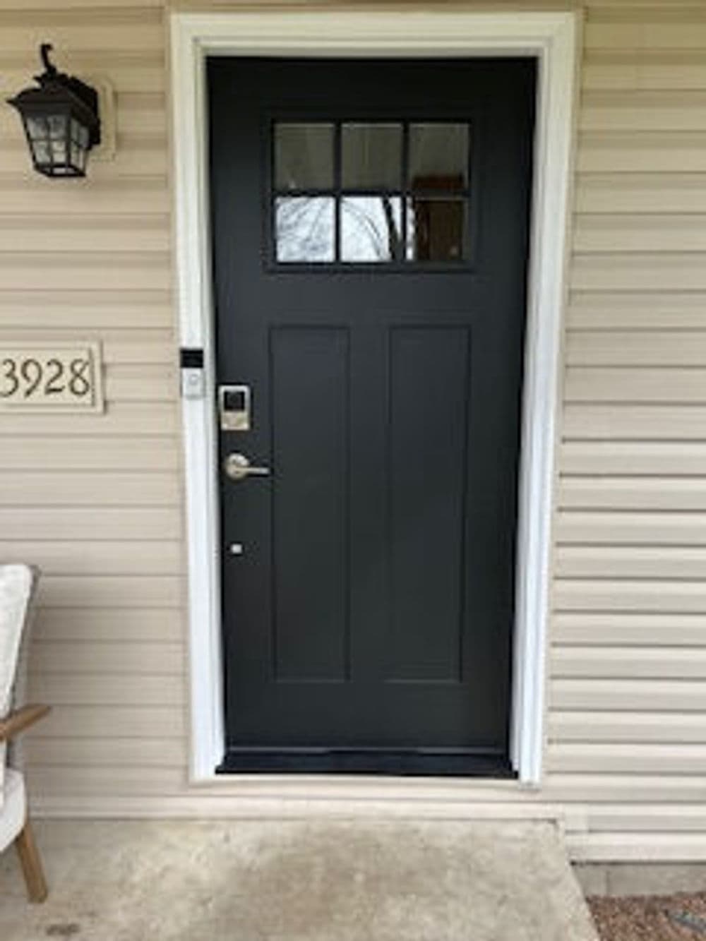 Modern black front door with glass panel, surrounded by cream siding and porch light.