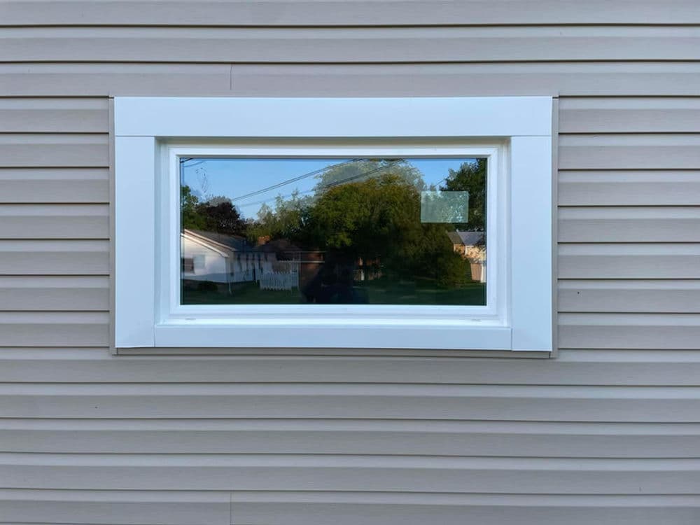 Modern window set in beige siding, offering a view of a green landscape outside.