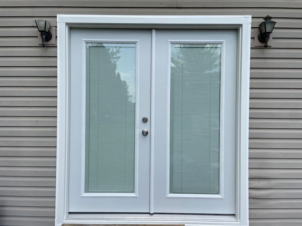 Double glass door with vertical blinds, framed in white, on a textured beige wall.