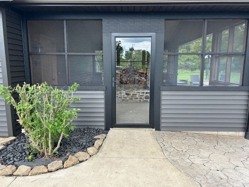 Screened porch entrance with stone detailing, green shrub, and gray siding.