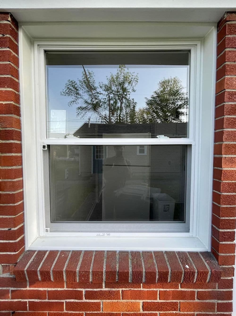 Modern double-hung window with a brick frame, reflecting nearby trees and houses.
