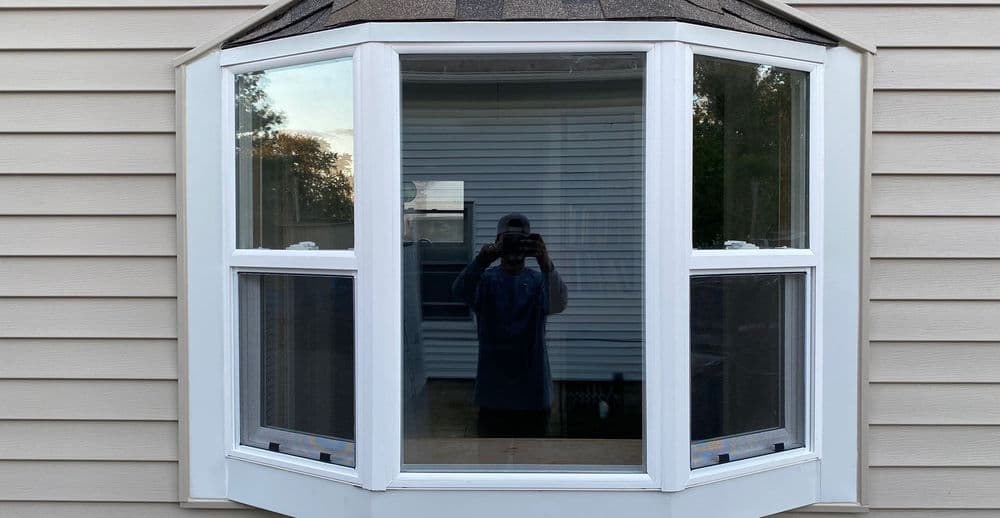 Bay window with a glass reflection, showcasing a house's exterior and siding details.