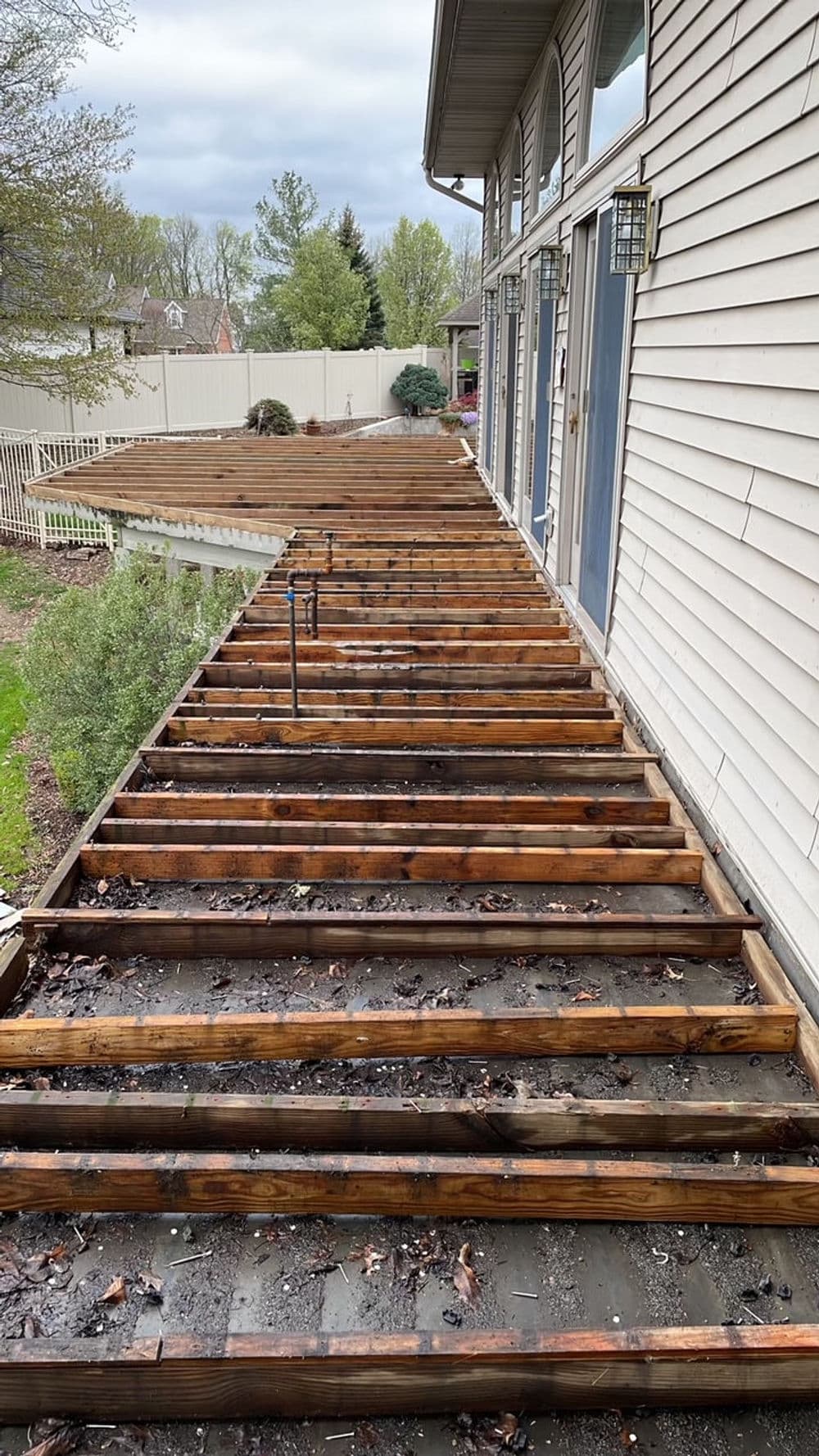 Deck repair project with removed planks, showing wooden beams and outdoor space.