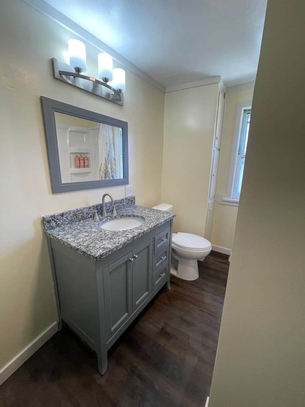 Modern bathroom with gray vanity, granite countertop, mirror, and stylish lighting. Bright and inviting.