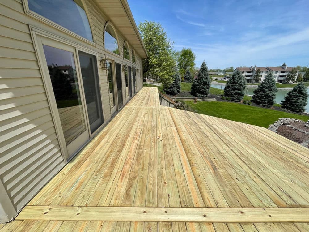 Spacious wooden deck with a view of landscaped yard and pine trees on a sunny day.