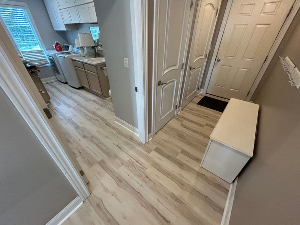 Spacious hallway with light brown laminate flooring, leading to a modern kitchen and storeroom.