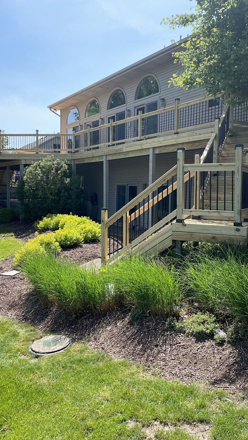 Spacious house with a large deck and new wooden stairs, surrounded by lush greenery.